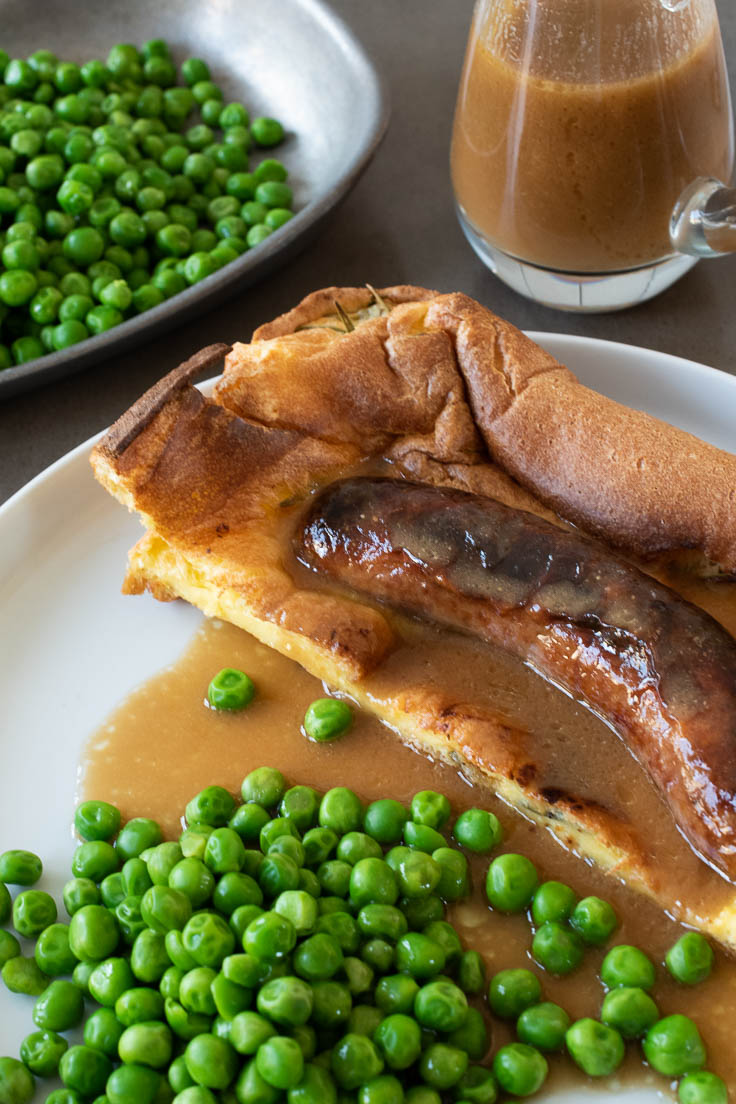A closeup showing the browned sausage inside the batter with gravy and peas