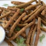 Long green beans that are fried, stacked on a board with a dipping sauce