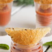 A crispy, small grilled cheese placed inside a shot glass of tomato soup