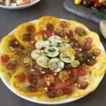 Sliced yellow and red heirloom tomatoes with sliced zucchini on a round plate