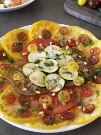 Sliced yellow and red heirloom tomatoes with sliced zucchini on a round plate