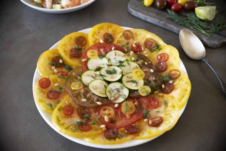 Sliced yellow and red heirloom tomatoes with sliced zucchini on a round plate