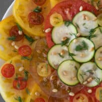 Thin slices of yellow and red tomato with sliced zucchini topped with fresh dill, pine nuts and flaky sea salt.