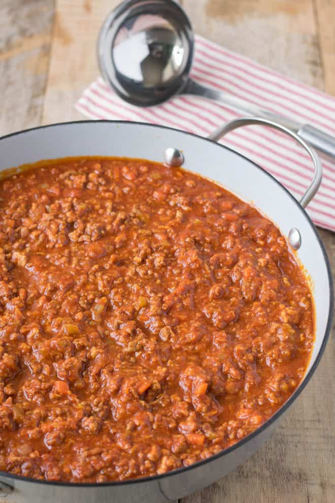 A large pan of Bolognese sauce with a ladle