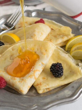 Thin pancakes on a plate served with syrup and fruit