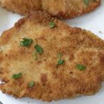 A close-up of a breaded chicken breast garnished with parsley