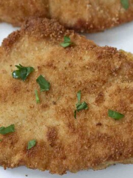 A close-up of a breaded chicken breast garnished with parsley