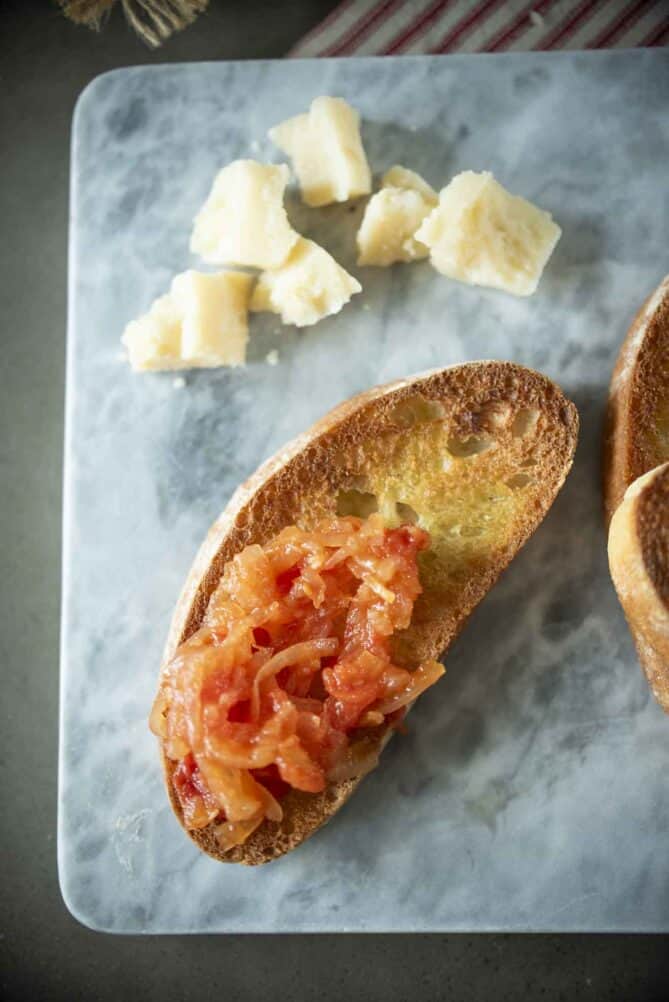 Crostini topped with onion and tomato with chunks of Parmesan cheese.