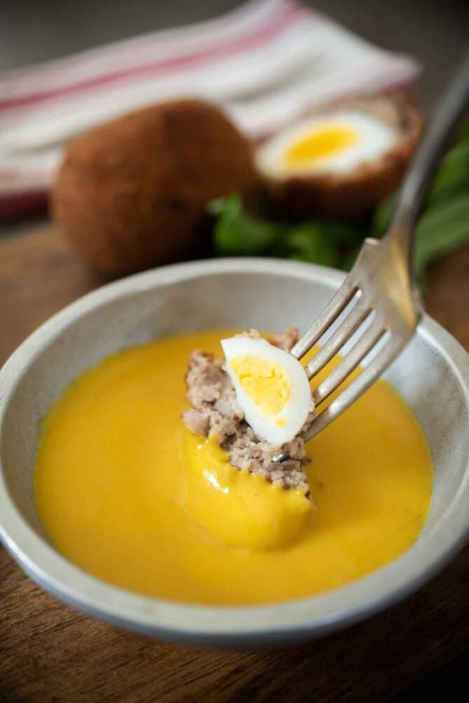 Dipping a bite of Scotch egg into mustard sauce