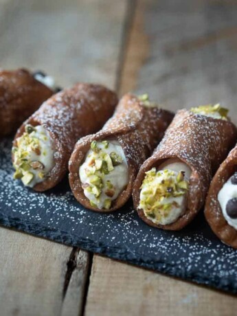 5 cannoli on a board dusted with powdered sugar