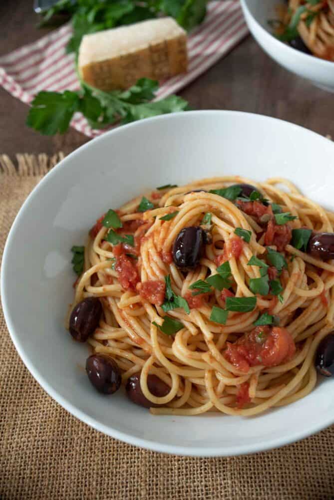 A closeup of spaghetti puttanesca with kalamata olives, tomato and chopped parsley