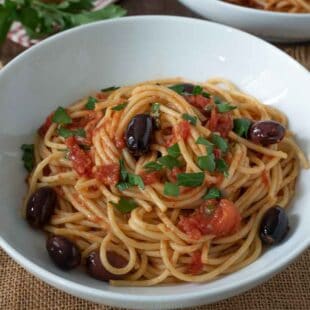 Shiny black olives, tomato and parsley with spaghetti in a white bowl