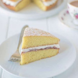 A slice of sponge cake sandwiched with cream and jam on a plate with a fork