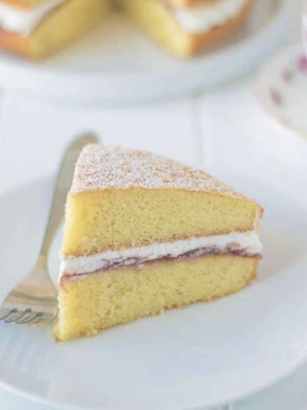 A slice of sponge cake sandwiched with cream and jam on a plate with a fork