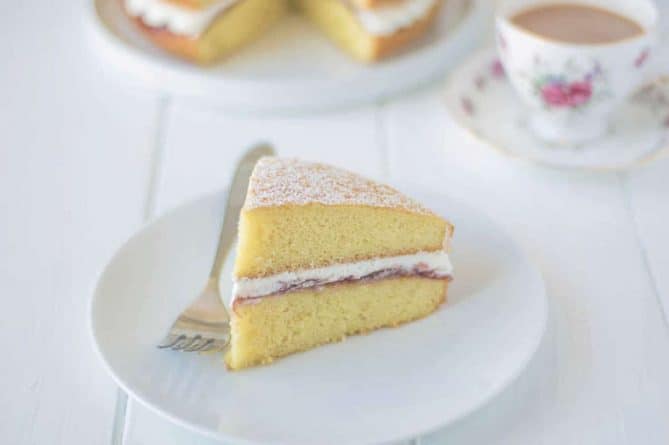 A slice of sponge cake sandwiched with cream and jam on a plate with a fork
