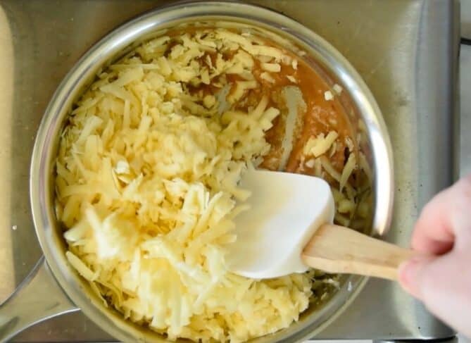 Stirring white grated cheddar cheese into a sauce