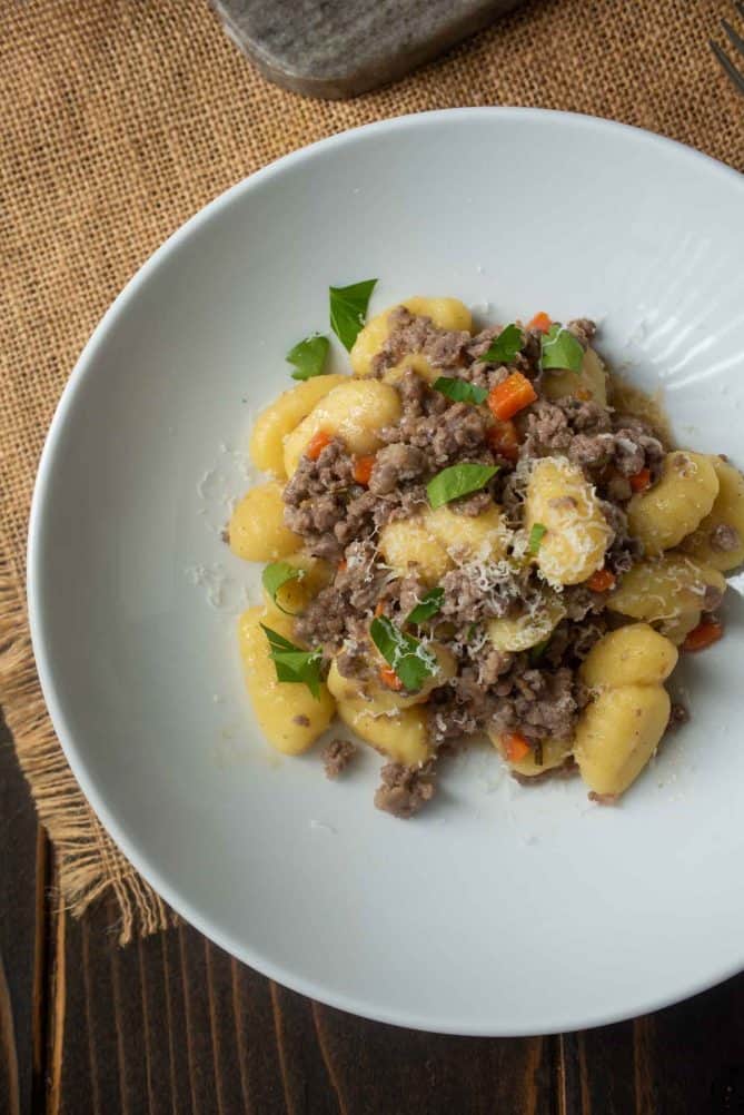 A closeup of meat sauce and gnocchi on a white plate garnished with chopped parsley