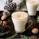 Eggnog in glass mugs surrounded by shelled nuts, pine cones and fern
