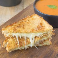 A triple grilled cheese sliced in half showing the melted cheese inside on a serving board with tomato basil soup