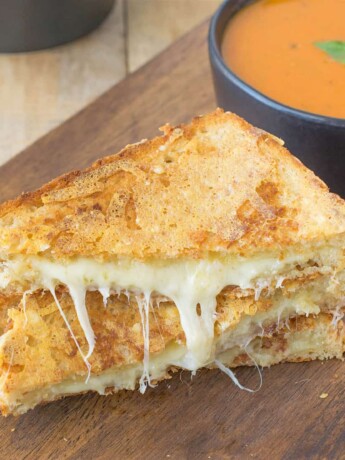 A triple grilled cheese sliced in half showing the melted cheese inside on a serving board with tomato basil soup