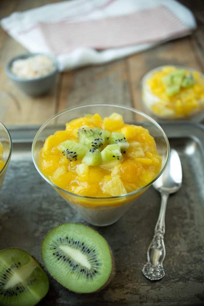 A martini shaped glass with rice pudding, mango, pineapple and kiwi on a tray with a spoon