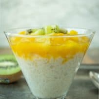 A glass filled with rice pudding viewed from the side showing the rice in the creamy sauce topped with sauced mango and pineapple