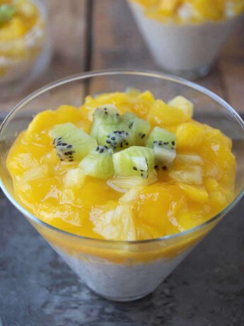 Tropical rice pudding in a coned shape glass topped with fresh mango, kiwi and pineapple with a spoon and extra kiwi