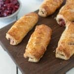 Turkey, stuffing and cranberry sausage rolls are served on a board with a side of cranberry sauce and peas
