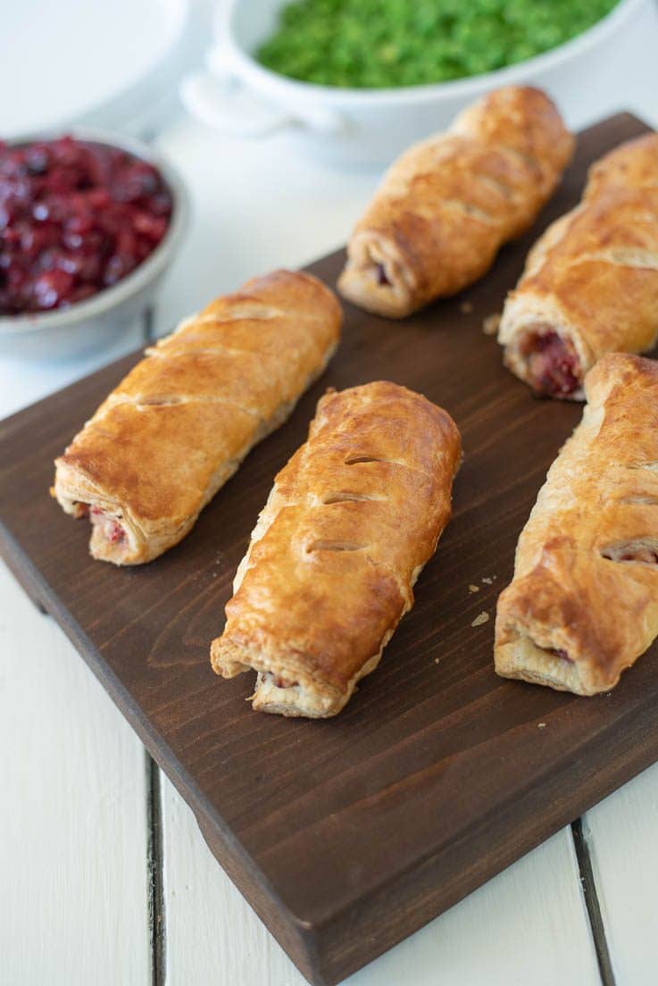 Turkey, stuffing and cranberry sausage rolls are served on a board with a side of cranberry sauce and peas