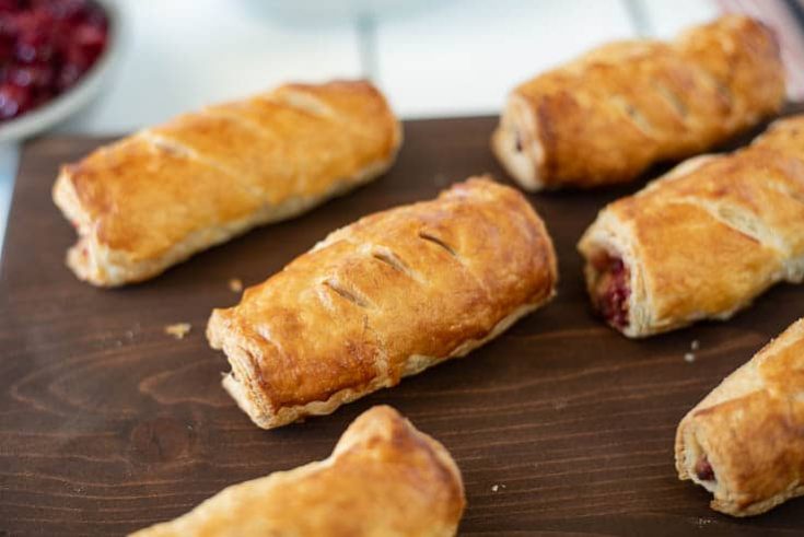 Turkey, stuffing and cranberry sausage rolls lined up on a wooden board