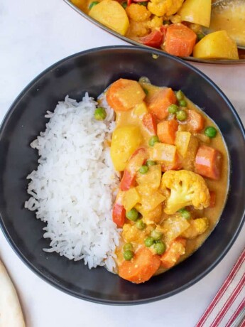 A black bowl filled with white rice and vegetable curry