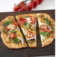 Vegetale pesto flatbread pizza cut into 3 slices on a board with cherry tomatoes on the vine