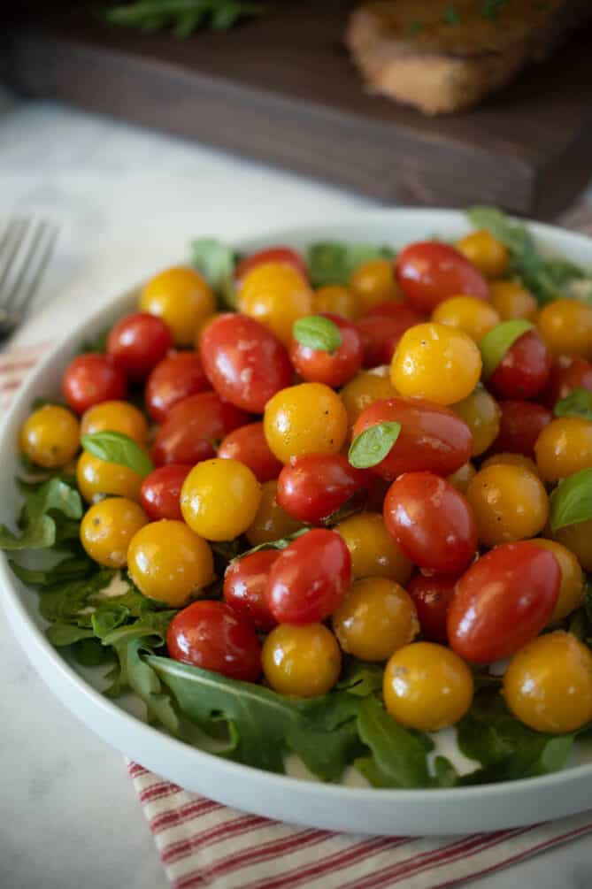 A closeup of red and yellow cherry tomatoes with small fresh basil leaves