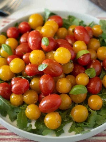 Red and yellow cherry tomatoes served warm on a plate with greens and basil