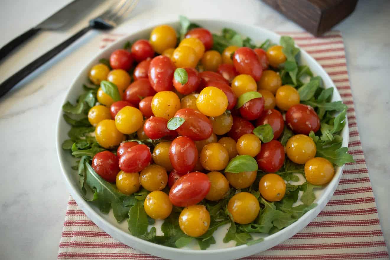 Red and yellow cherry tomatoes served warm on a plate with greens and basil