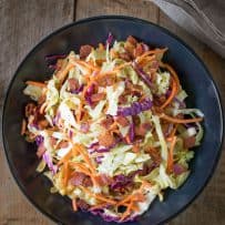 A black bowl filled with colorful warm bacon coleslaw