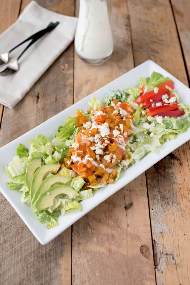 A bed of lettuce topped with buffalo chicken, peppers, avocado, blue cheese and dressing.