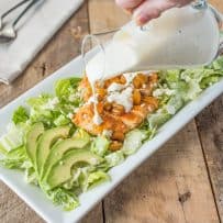Pouring blue cheese dressing over buffalo chicken salad