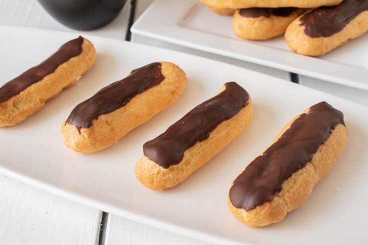 4 eclairs lined up on a plate with more in the background