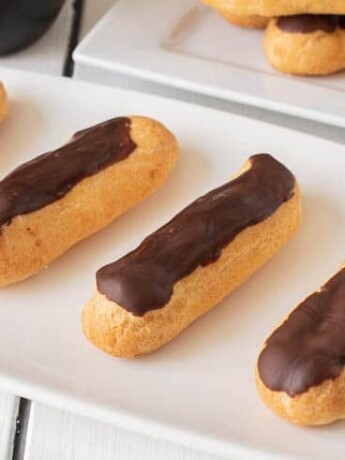 4 eclairs lined up on a plate with more in the background