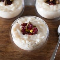 3 glass bowls of white chocolate rice pudding topped with dried cranberries and pistachios