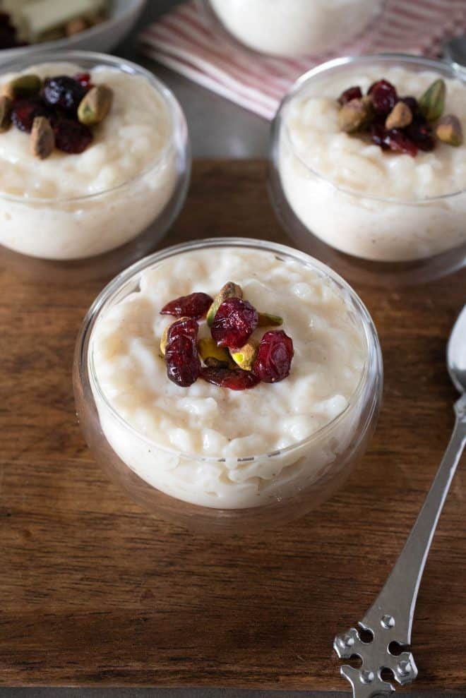3 glass bowls of white chocolate rice pudding topped with dried cranberries and pistachios