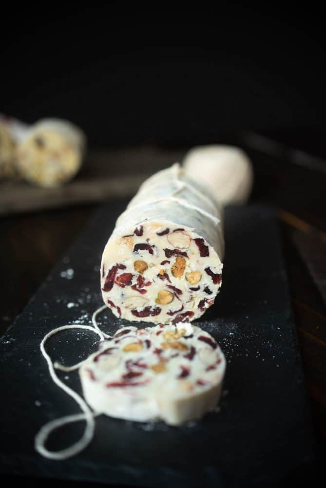 A sliced white chocolate salami showing the nuts and dried cranberries inside.