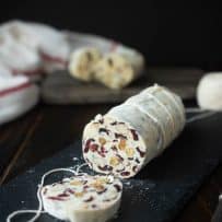 White chocolate salami wrapped in string and cut open with dried cranberries and nuts inside