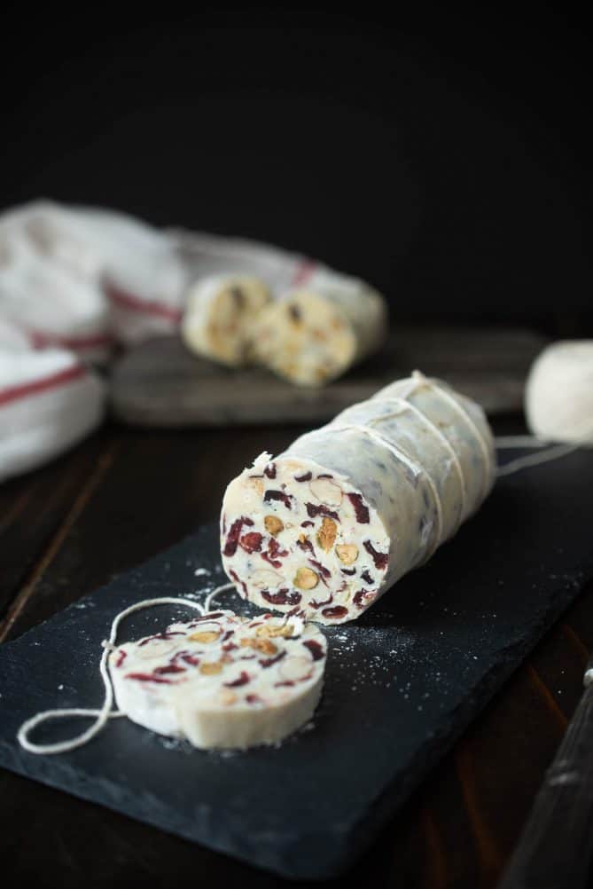 White chocolate salami wrapped in string and cut open with dried cranberries and nuts inside