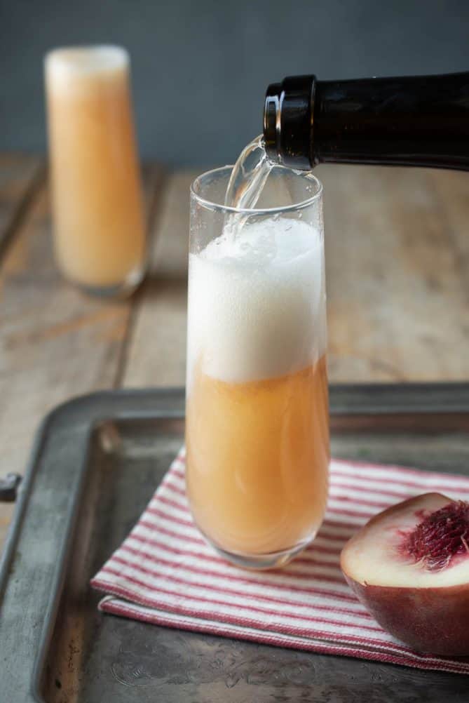 Pouring Prosecco into a glass with peach puree with a foamy top