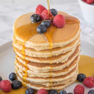 A large stack of pancakes topped with fruit pouring over syrup