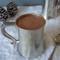 Belgian hot chocolate in a grey mug in snow with a spoon and pine cones