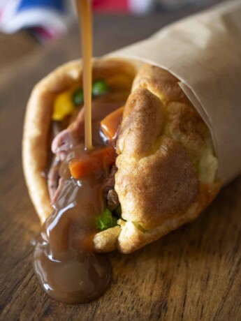 Pouring gravy over roast beef and vegetables wrapped in a Yorkshire pudding