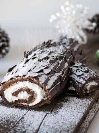 The side view of a chocolate yule log showing the cream filling and dusting of powdered sugar falling like snow